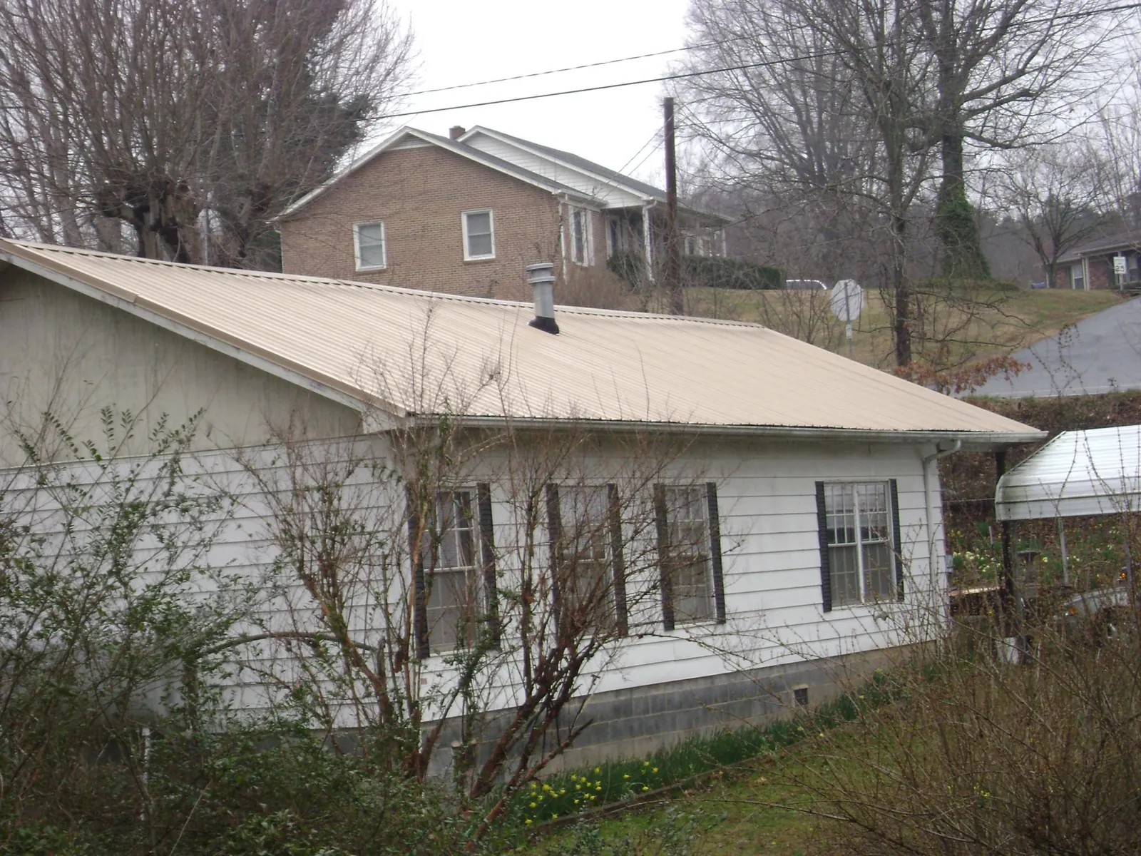 Tan metal roof on a white sided house set into a hillside — Commercial Roofing by Roofing Brothers in Wayland