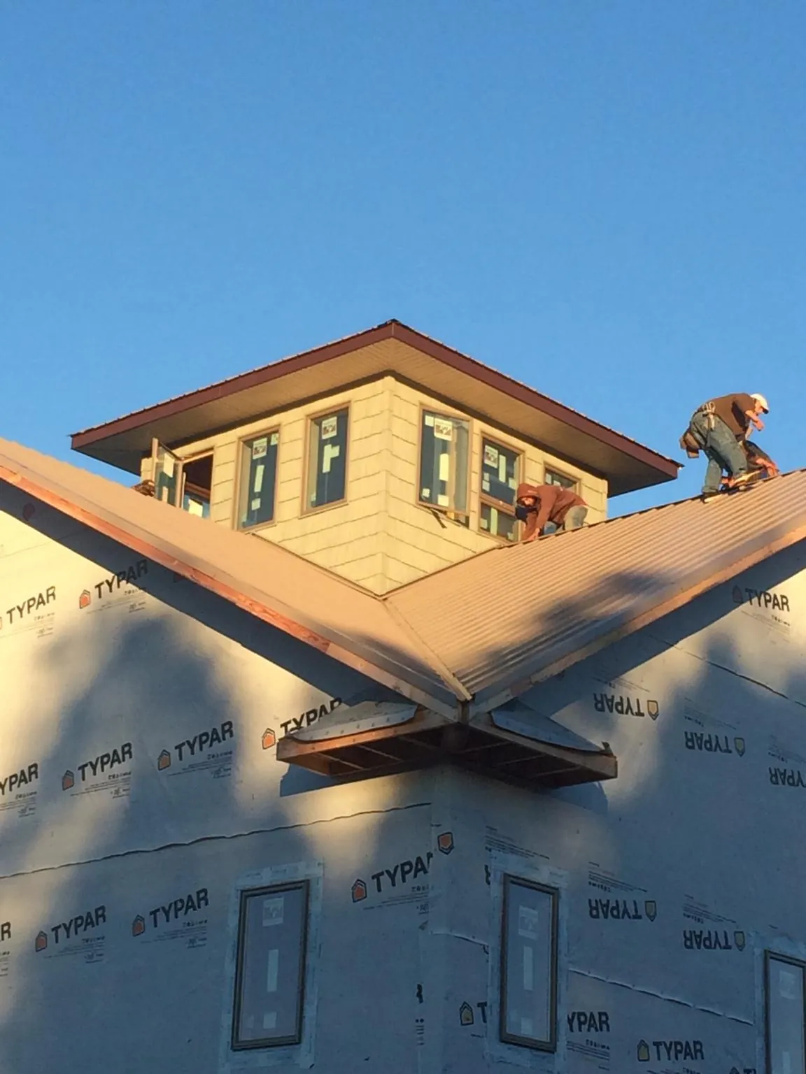 Roofers working around a rooftop cupola on a new metal roof at sunset — Roof Waterproofing in Wayland by Roofing Brothers